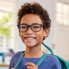 Young boy wearing glasses smiling as he poses for a photo in his classroom at school